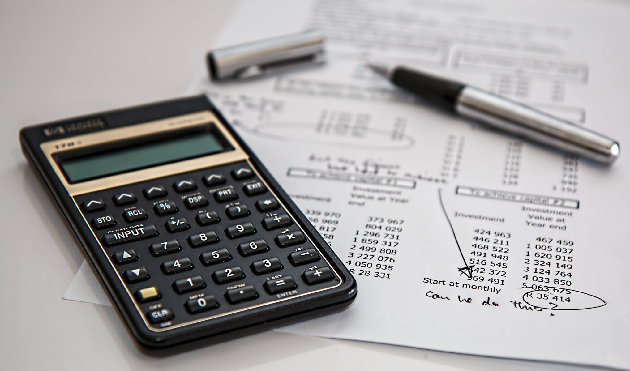 Black and White Calculator Beside a Pen and white paper